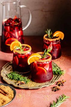 three glasses filled with red liquid and garnished with orange slices, cinnamon sticks and rosemary