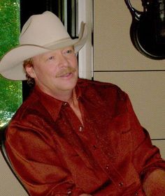 a man wearing a cowboy hat sitting in a chair with his hands on his hips