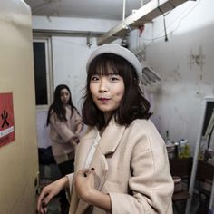 a woman in a coat and hat standing next to a door with another person behind her