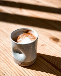 a white cup filled with liquid sitting on top of a wooden table