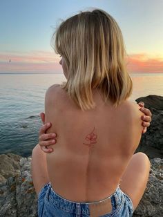 a woman sitting on top of a rock next to the ocean with her back turned