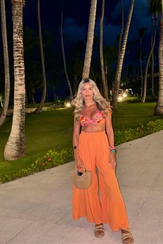 a woman standing in front of palm trees wearing an orange skirt and matching top with sandals