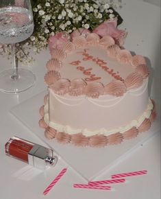 a pink cake sitting on top of a table next to a wine glass and lipstick