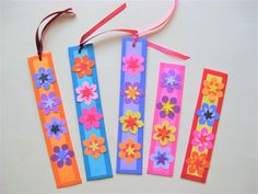 four bookmarks with flowers on them are hanging from ribbons and tied to the wall