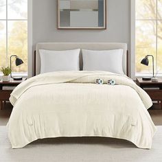 a bed with white sheets and pillows in a bedroom next to two lamps on the nightstands