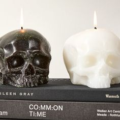 two candles that are on top of some books and one has a skull in the middle