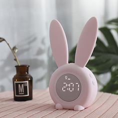 a pink alarm clock sitting on top of a table next to a vase with a flower