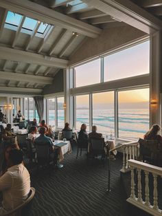 people sitting at tables in front of large windows overlooking the ocean