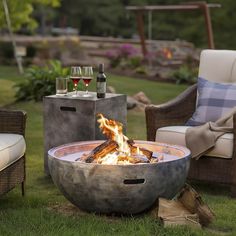 a fire pit sitting on top of a grass covered field next to chairs and tables