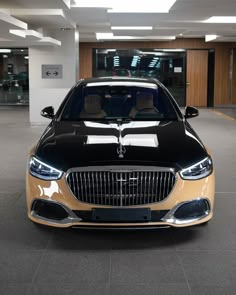 the front end of a black and gold car in a showroom with lights on