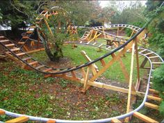 a wooden roller coaster in the middle of a park with lots of trees and grass