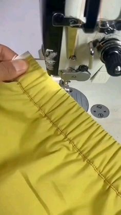 someone is sewing something on a machine with yellow material in the foreground and another person's hand