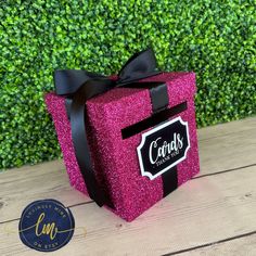 a pink gift box with black ribbon and name on it