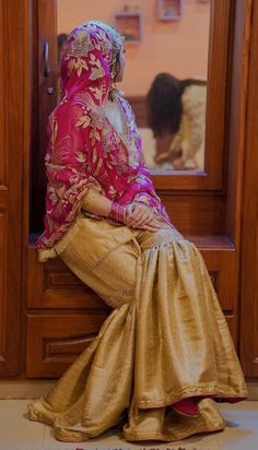 a woman in a pink and gold sari sitting on the door way to her home