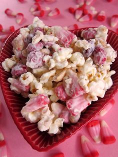 a red heart shaped bowl filled with white and pink candy caned popcorn kernels