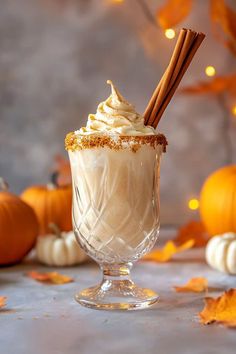 a glass filled with whipped cream surrounded by pumpkins and cinnamon sticks on a table