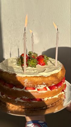 a cake with strawberries and candles on it is being held by someone's hand