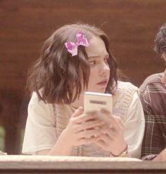 two people sitting at a table looking at a cell phone with a pink bow in their hair