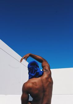 a man with no shirt on standing in front of a white wall and wearing a blue hoodie