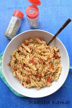 a white bowl filled with pasta on top of a blue table next to tomatoes and seasoning