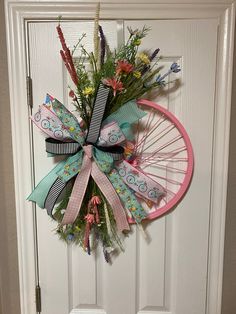 a door hanger with flowers and ribbons on it's front wheel, hanging from the side of a white door