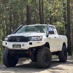 a white truck parked in the middle of a forest with large tires on it's sides