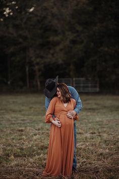 a pregnant woman in an orange dress and cowboy hat hugs her husband's forehead