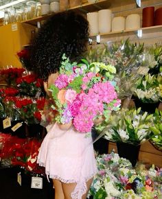 a woman holding a bouquet of flowers in front of a flower shop display filled with lots of different types of flowers