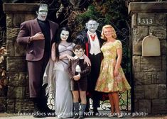 a family dressed up as the addams posing for a photo in front of an iron gate