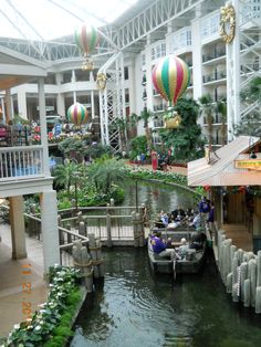 people are riding in a boat on the water inside an indoor shopping mall with hot air balloons hanging from the ceiling