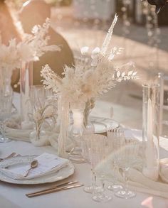 the table is set with clear vases and silverware, plates and utensils