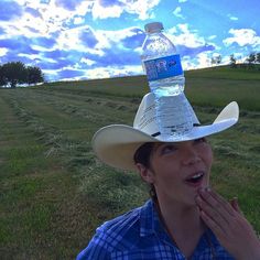 a woman wearing a cowboy hat with a water bottle on her head in the middle of a field