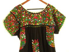 a black top with colorful flowers on it hanging from a wooden hanger and a white background