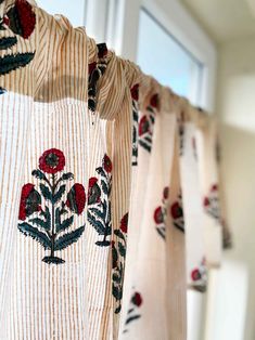 the curtains are decorated with red flowers and black leaves on white fabric, hanging from a window sill