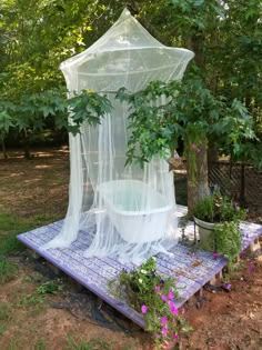 a white bed sitting in the middle of a lush green forest next to a potted plant