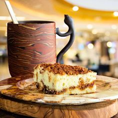 a piece of cake sitting on top of a wooden plate next to a coffee cup