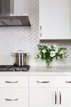 a white kitchen with stainless steel appliances and marble backsplash, flowers on the stove