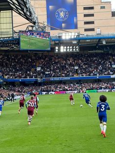 a group of people playing soccer on a field in front of an audience at a stadium