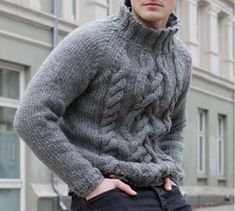 a young man wearing a gray sweater and black pants standing in front of a building