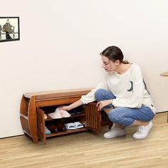 a woman kneeling on the floor in front of a wooden cabinet with shoes inside it