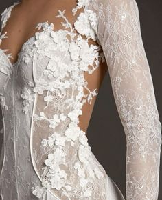 the back of a woman's wedding dress with sheer sleeves and flowers on it