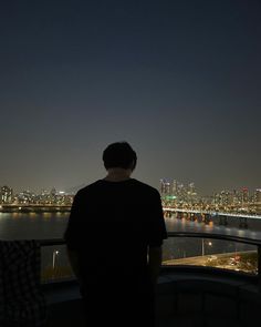 a man standing on top of a tall building next to a body of water at night