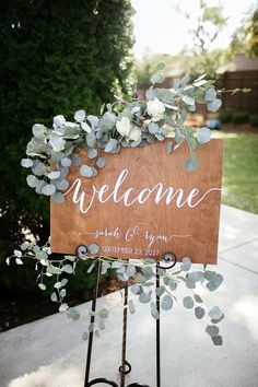 a wooden welcome sign sitting on top of a metal stand next to a tree and bushes