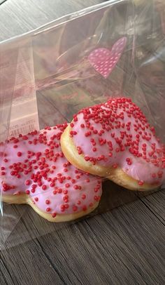 two donuts with pink icing and sprinkles in a clear plastic bag