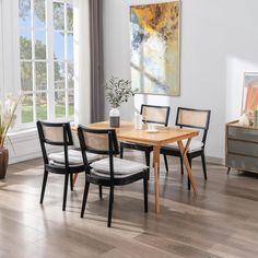 a dining room table with chairs and a painting on the wall behind it in front of a window