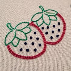 two embroidered strawberries sitting next to each other on a piece of white fabric with green and red thread