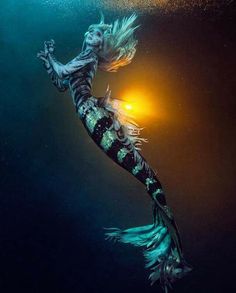 a woman is swimming under the water with her hair blowing in the wind and light shining on her face