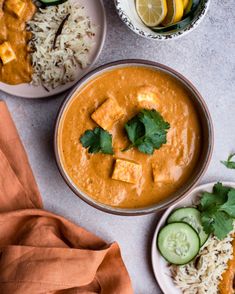 two bowls filled with curry, rice and cucumber slices next to each other