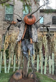 a scarecrow statue in front of a brick building with pumpkins on the ground