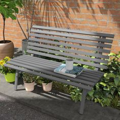 a wooden bench sitting in front of a brick wall next to potted planters